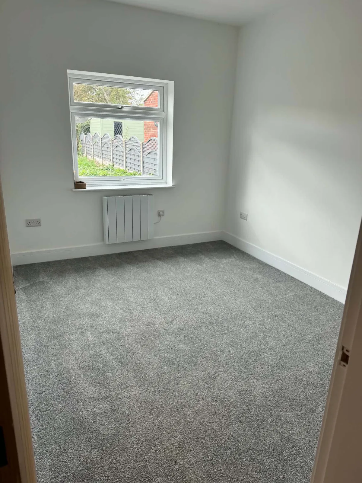 Bedroom with grey carpet, painted walls and a timber door in the Bassingham refurbishment